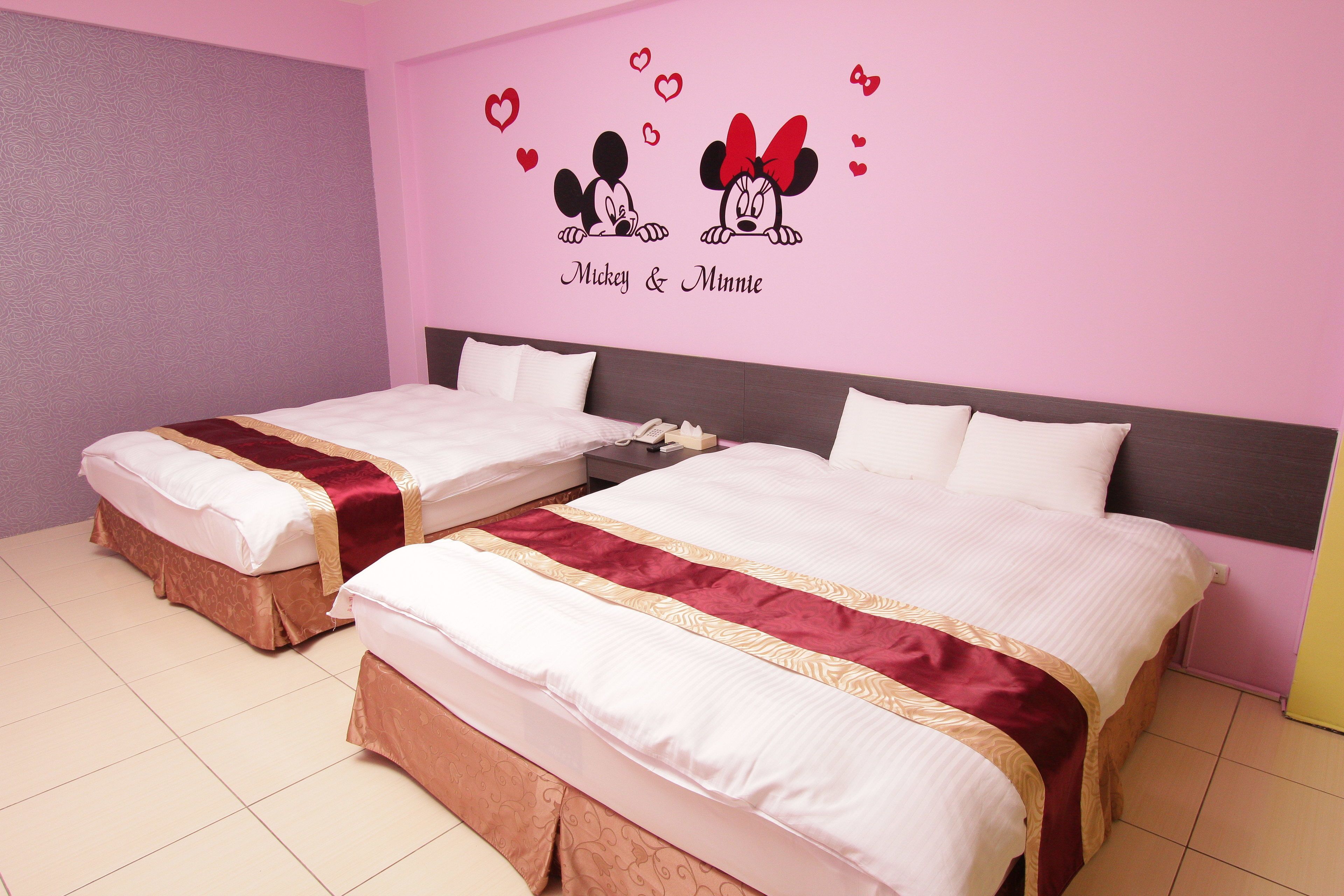 A hotel room with two beds, pink walls, and a Mickey & Minnie wall decal.