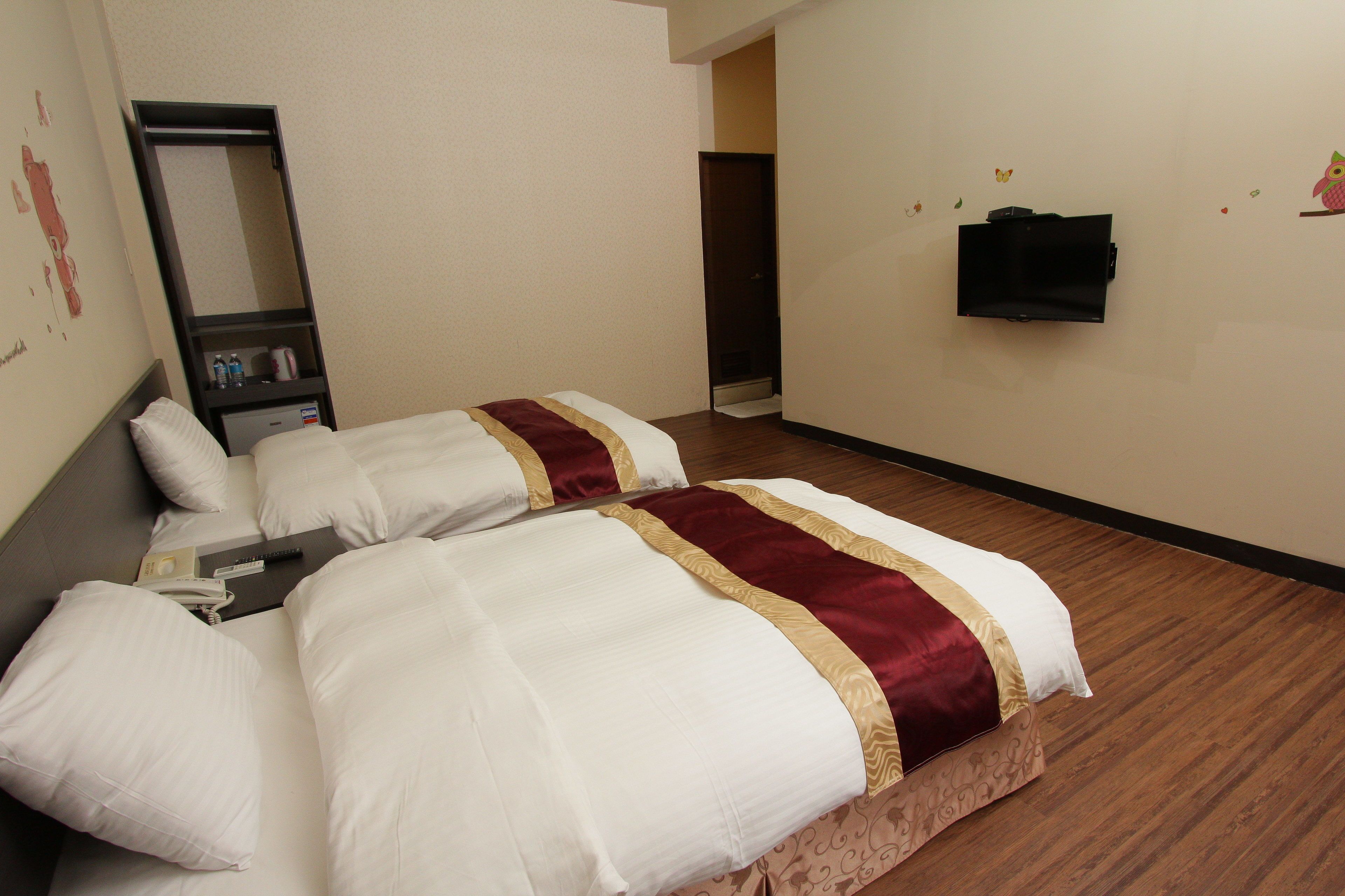 A hotel room with two beds, a mirror, a TV, and a small shelf with toiletries.