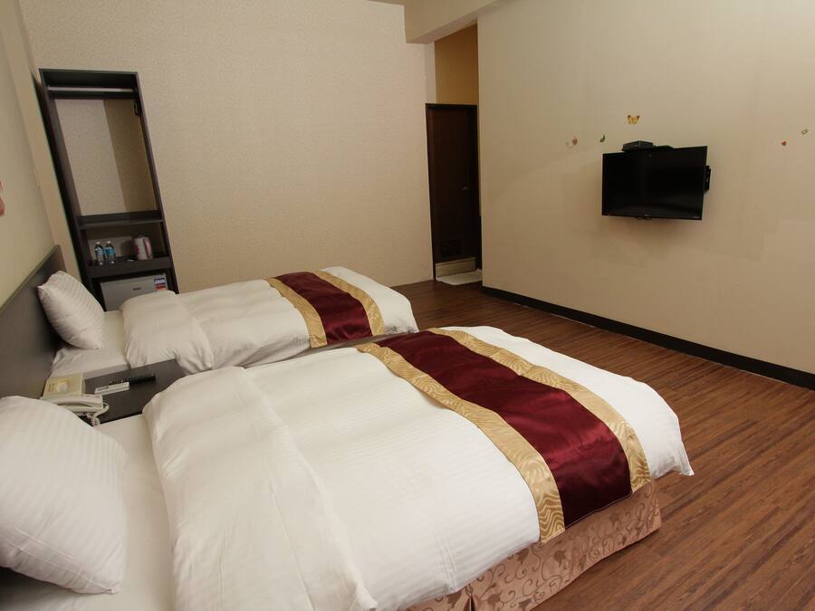 A hotel room with two beds, a mirror, a TV, and a small shelf with toiletries.