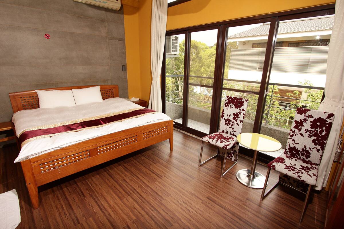 Una habitación de hotel con una cama de madera, una mesita redonda pequeña y dos sillas con tapicería floral.