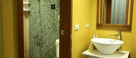 A bathroom with a tiled shower, a toilet, a sink with a mirror, and a cabinet.
