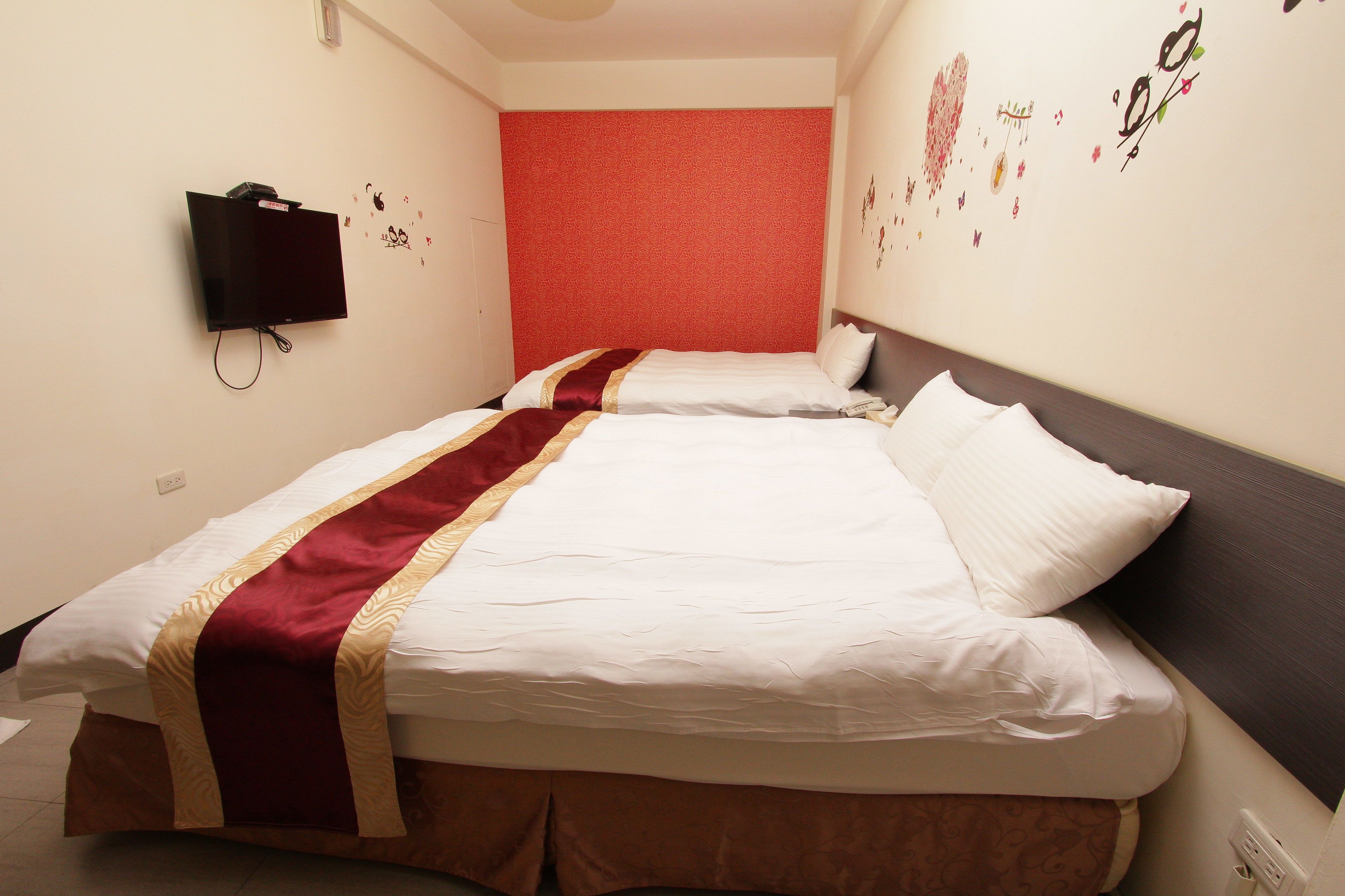 Une chambre d’hôtel avec deux lits, un téléviseur fixé au mur et des autocollants décoratifs sur les murs.