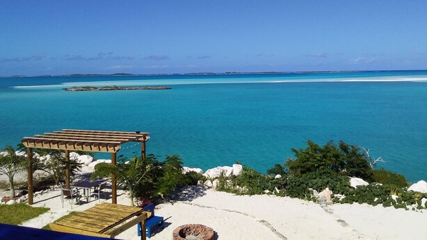 Vista de una playa con una pérgola de madera, zona de barbacoa y mar azul cristalino.