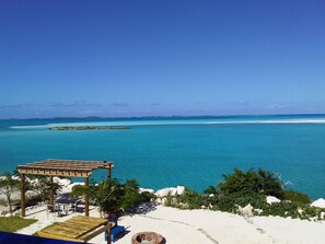 Blick auf einen Strand mit einer Holzpergola, einem Grillplatz und einem klaren, blauen Meer.