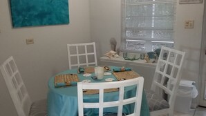 Un comedor con mantel turquesa, sillas blancas y un cuadro de delfines en la pared.