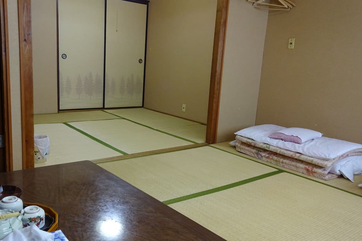 A traditional Japanese room with tatami flooring, a wooden table, and a futon bed with pillows.