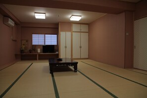 A traditional Japanese room with tatami flooring, a low table, a television, sliding doors, and a window with shoji screens. - Imazato Ryokan (Osaka)