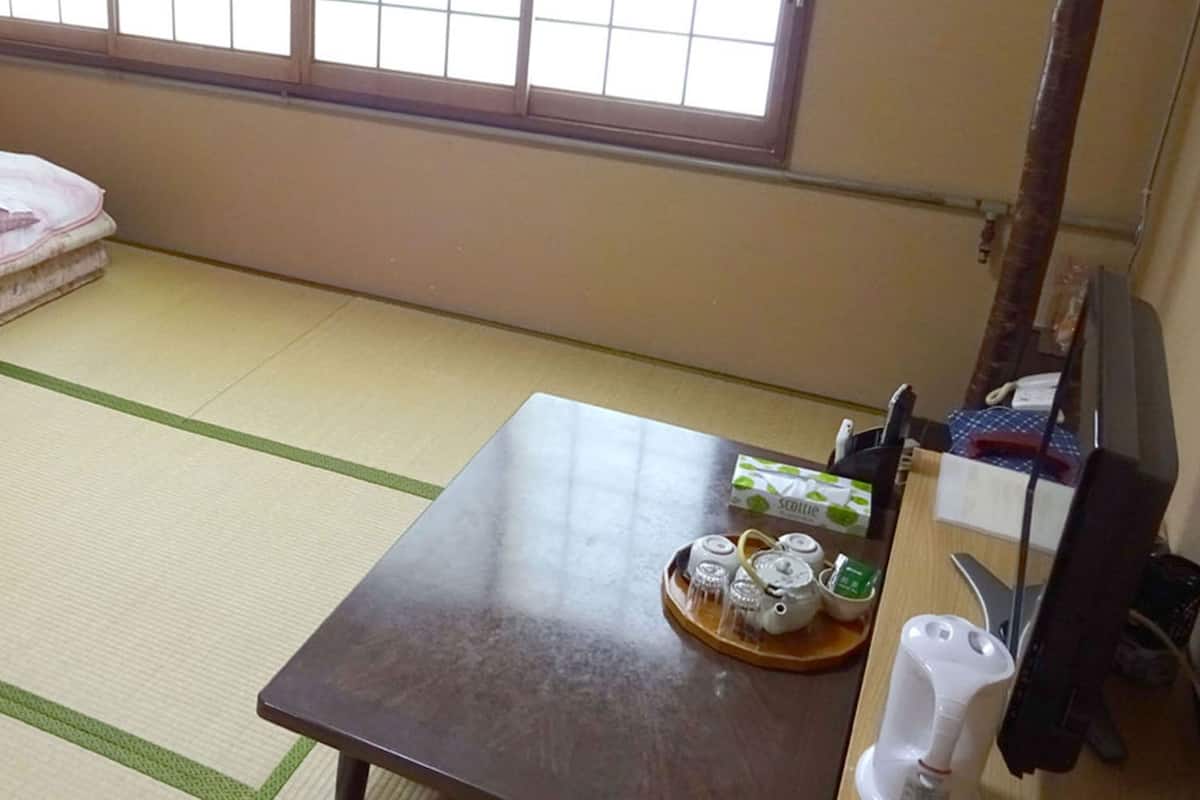 A tatami mat room with a bed, a table with tea sets, and a window.