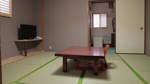 A traditional Japanese room with tatami flooring, a low table, a television on a shelf, and sliding doors. - Imazato Ryokan (Osaka)