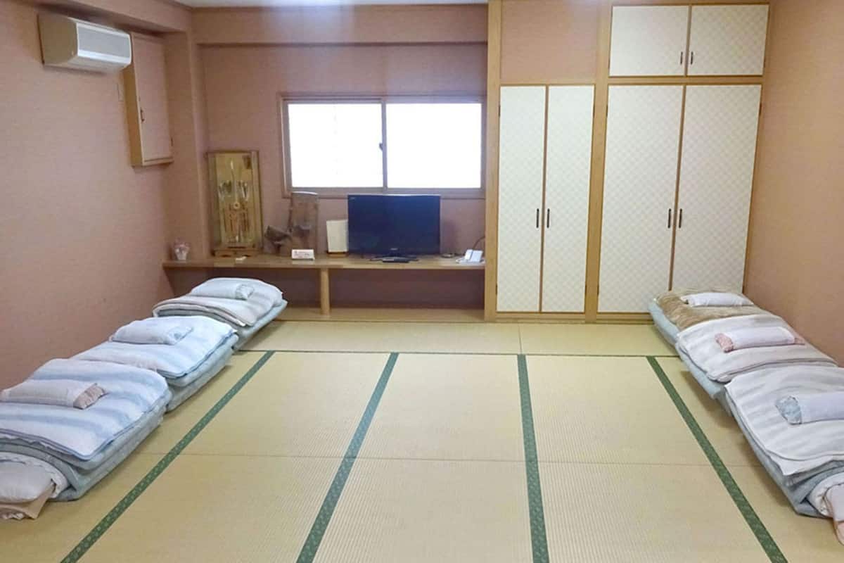 A room with two beds, a desk with a computer, a wardrobe, and a window.