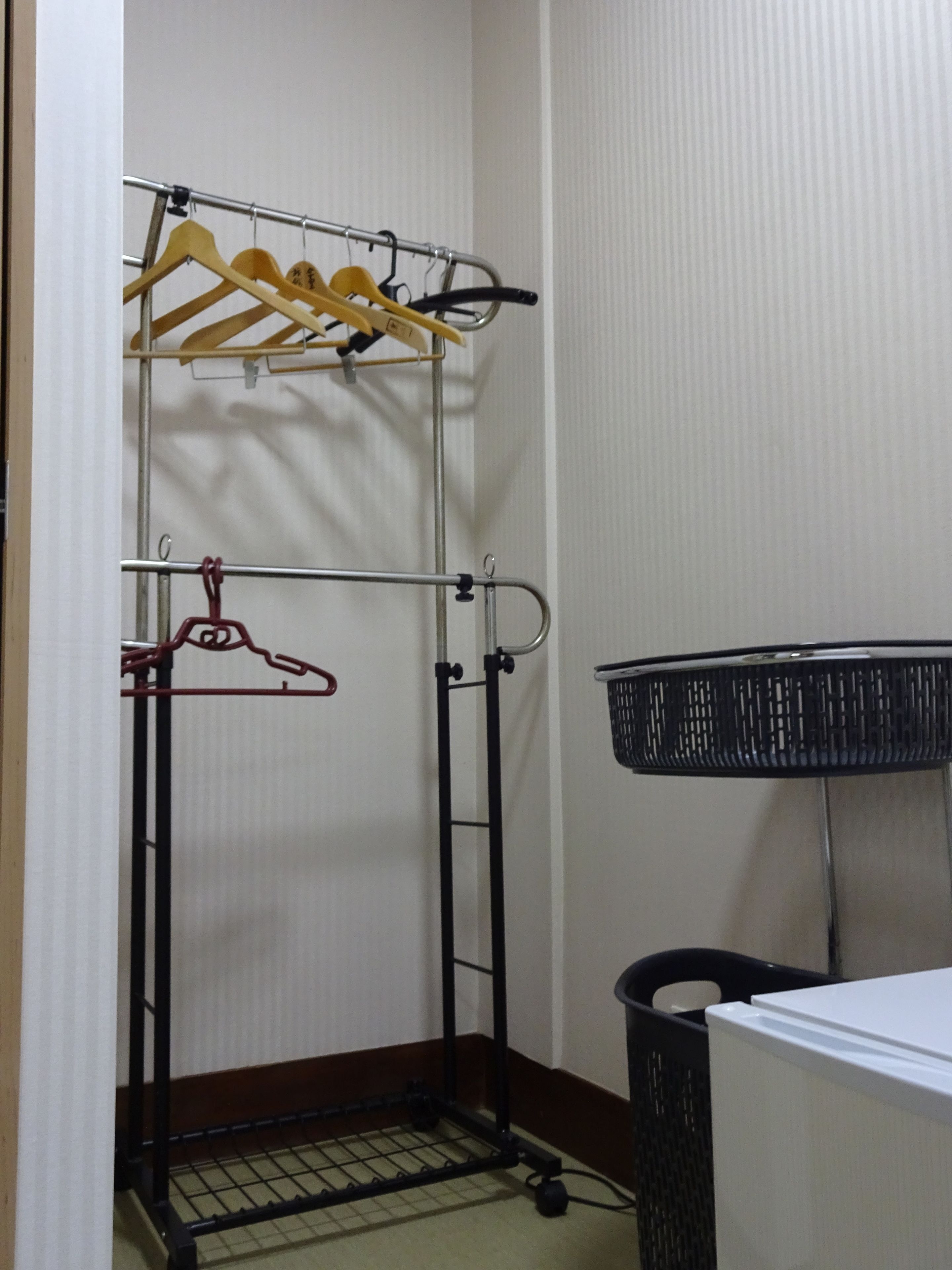 Um armário pequeno com um esguicho de metal, uma cesta de armazenamento preta e piso de azulejos.