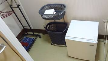 A compact room with a white refrigerator, two black baskets, a blue mat, and a white wall.