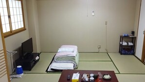 A traditional Japanese room with tatami flooring, a bed with folded bedding, a television, a small table with tea set, and a shelf with towels and toiletries. - Imazato Ryokan (Osaka)