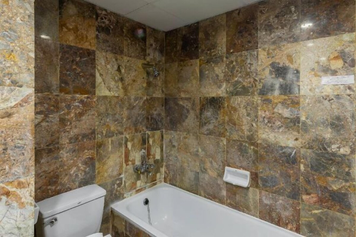 A bathroom with a toilet and a bathtub, marble walls, and a visible electrical outlet.