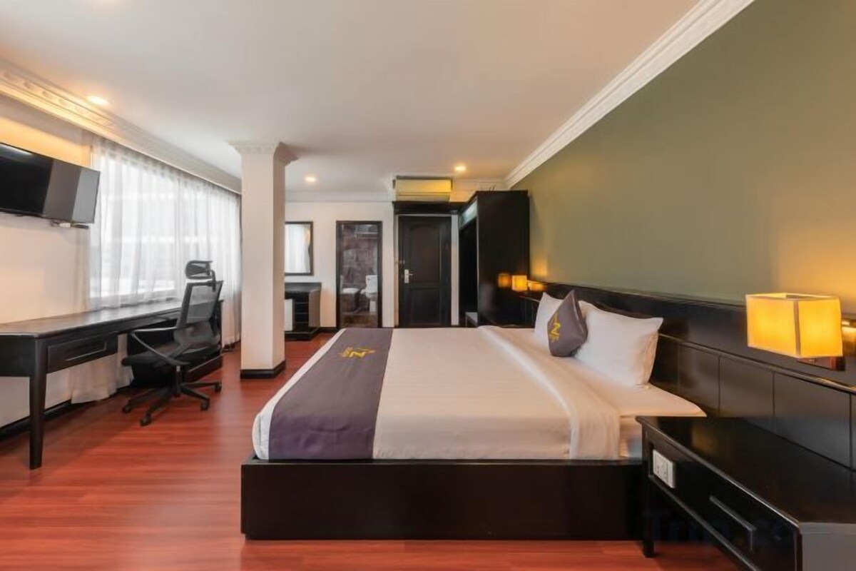 A hotel room with a bed, desk, chair, and a TV.
