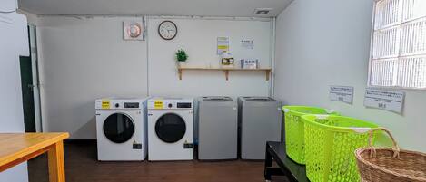 Une buanderie équipée de quatre machines à laver, d’un sèche-linge, d’une horloge et d’une étagère contenant divers objets.