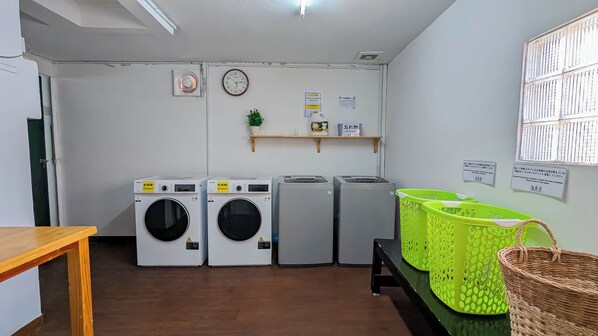A laundry room with four washing machines, a drying machine, a clock, and a shelf with items. - Azumaya Hotel Phnom Penh (Phnom Penh)