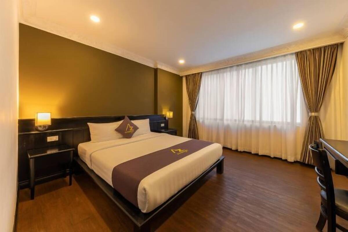 Ein Hotelzimmer mit Bett, Nachttischen, einem Schreibtisch und einem Fenster mit Vorhängen.