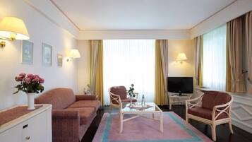 A hotel room with a sofa, two armchairs, a coffee table, a TV, and a small cabinet.