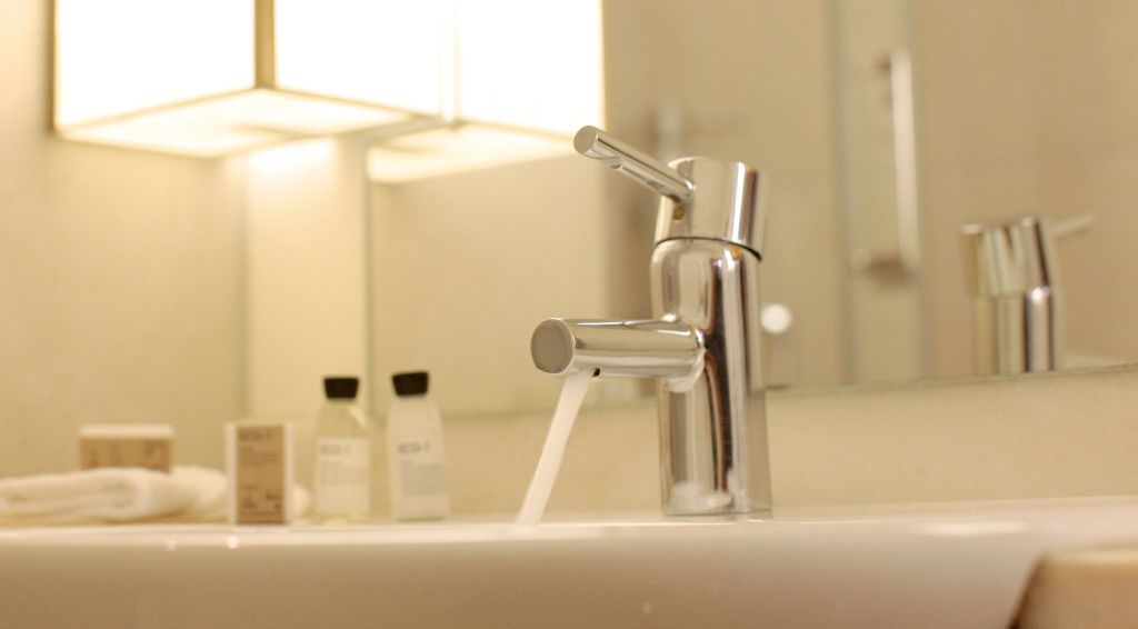 A bathroom sink with a chrome faucet and running water, a mirror above it, and toiletries on the counter.