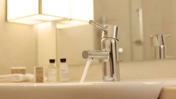 A bathroom sink with a chrome faucet and running water, a mirror above it, and toiletries on the counter.