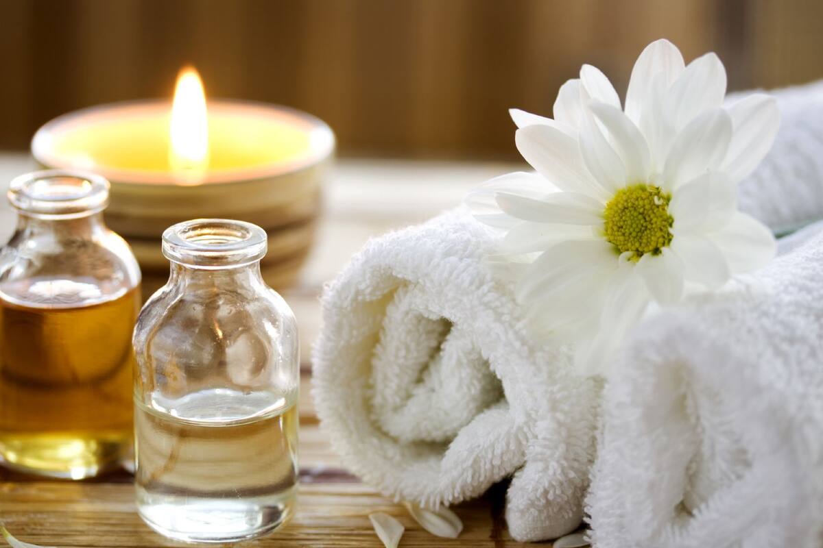 A candle, two glass bottles, and a rolled white towel with a white flower.