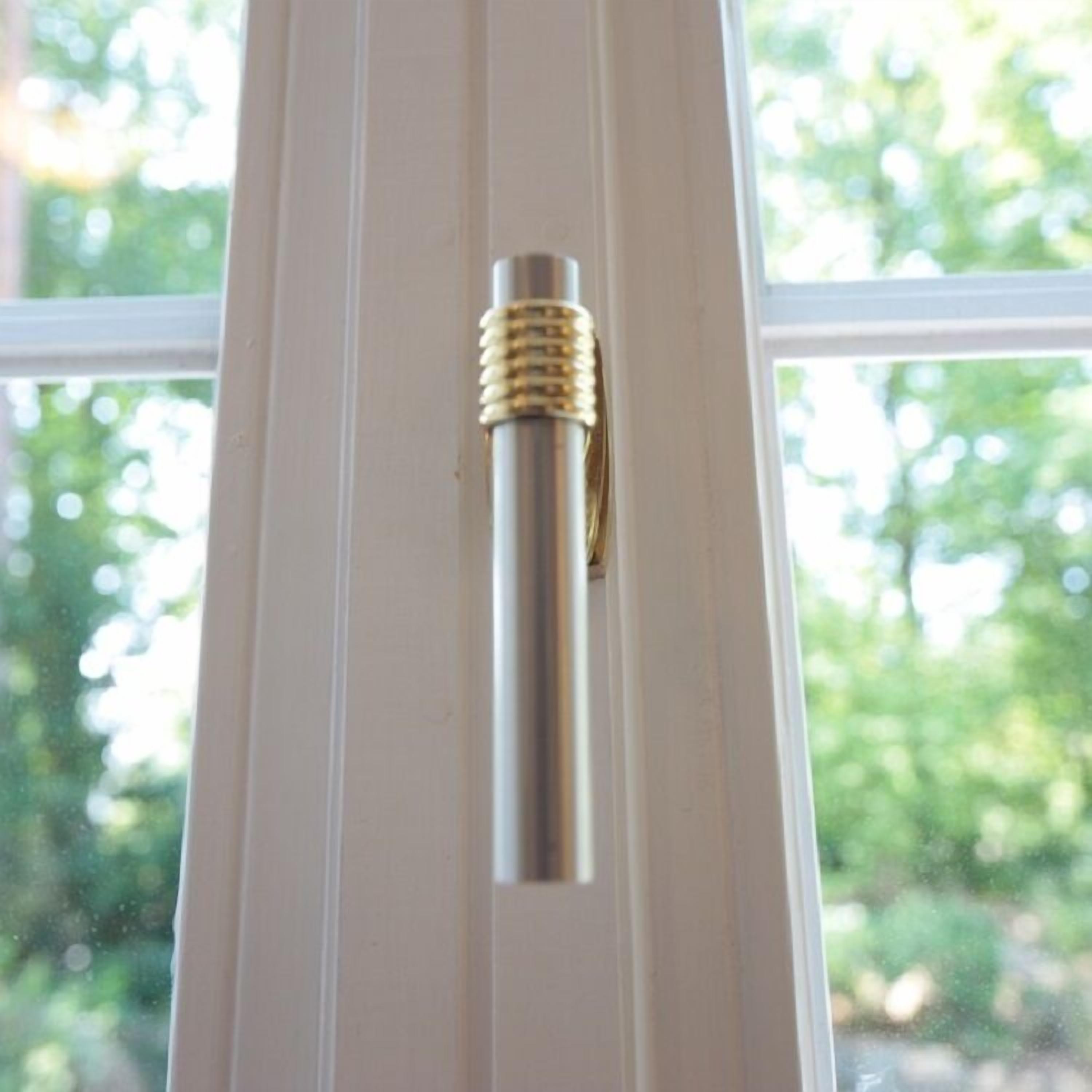 Un objeto metálico, posiblemente una herramienta, sujeto a un marco de ventana blanco.