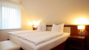 Habitación de hotel con una cama grande, dos mesitas de noche con lámparas, un banco y una ventana con persianas.