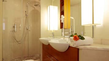A modern bathroom with a glass-enclosed shower, two sinks, a vanity with a mirror, and a towel with a rose on the counter.