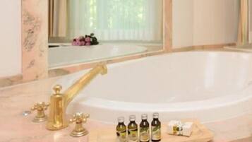 A bathroom with a marble sink, a large mirror, and a bathtub. There are bottles of toiletries on the sink.