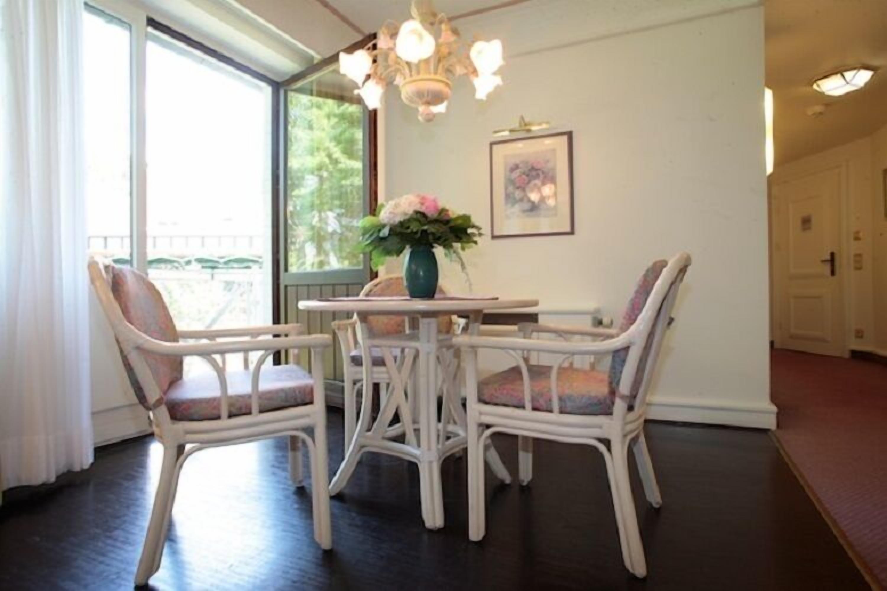 A dining area with a round table and four chairs, a vase with flowers, and a chandelier.
