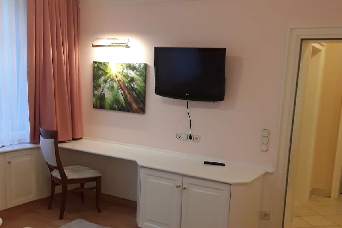 A hotel room with a bed, a desk with a TV, a chair, and a painting on the wall.