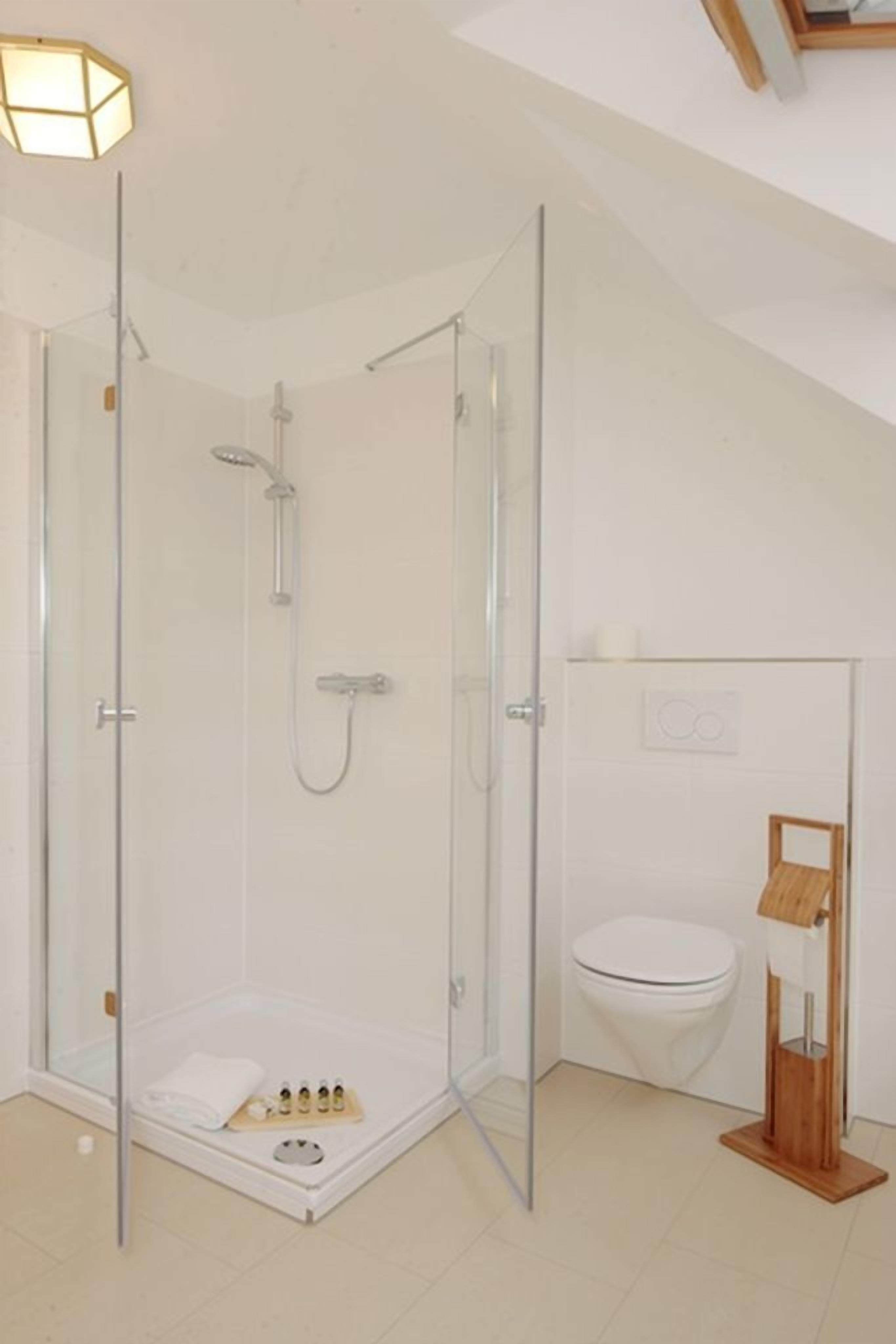 Un baño moderno con ducha de vidrio, inodoro y toallero de madera.