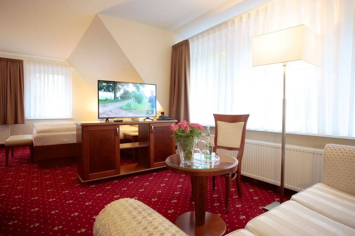 A hotel room with a bed, a TV, a small table with flowers, a chair, and a lamp.