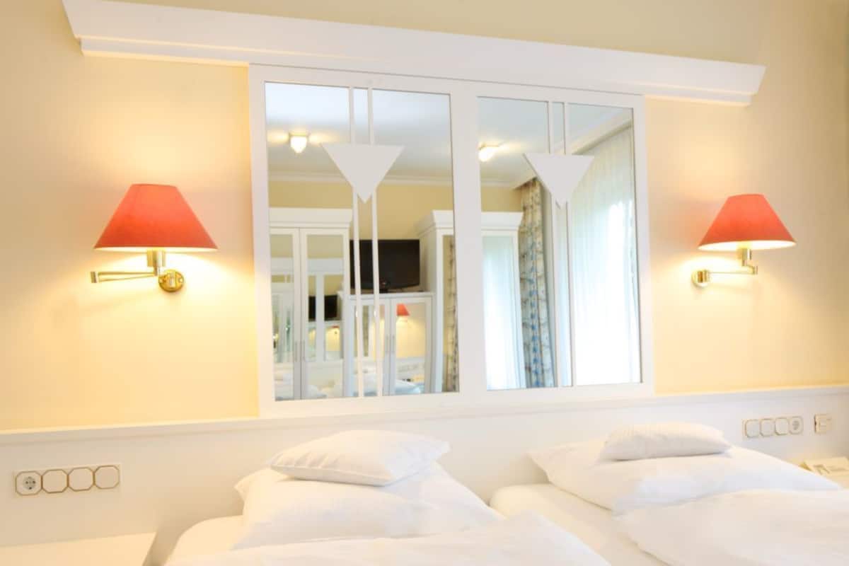 A hotel room with two beds, a large window with a view, and wall-mounted lamps.