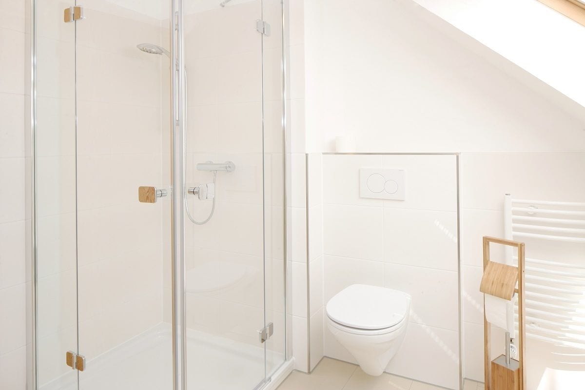 Un baño moderno con cabina de ducha de vidrio, inodoro blanco y toallero de madera.