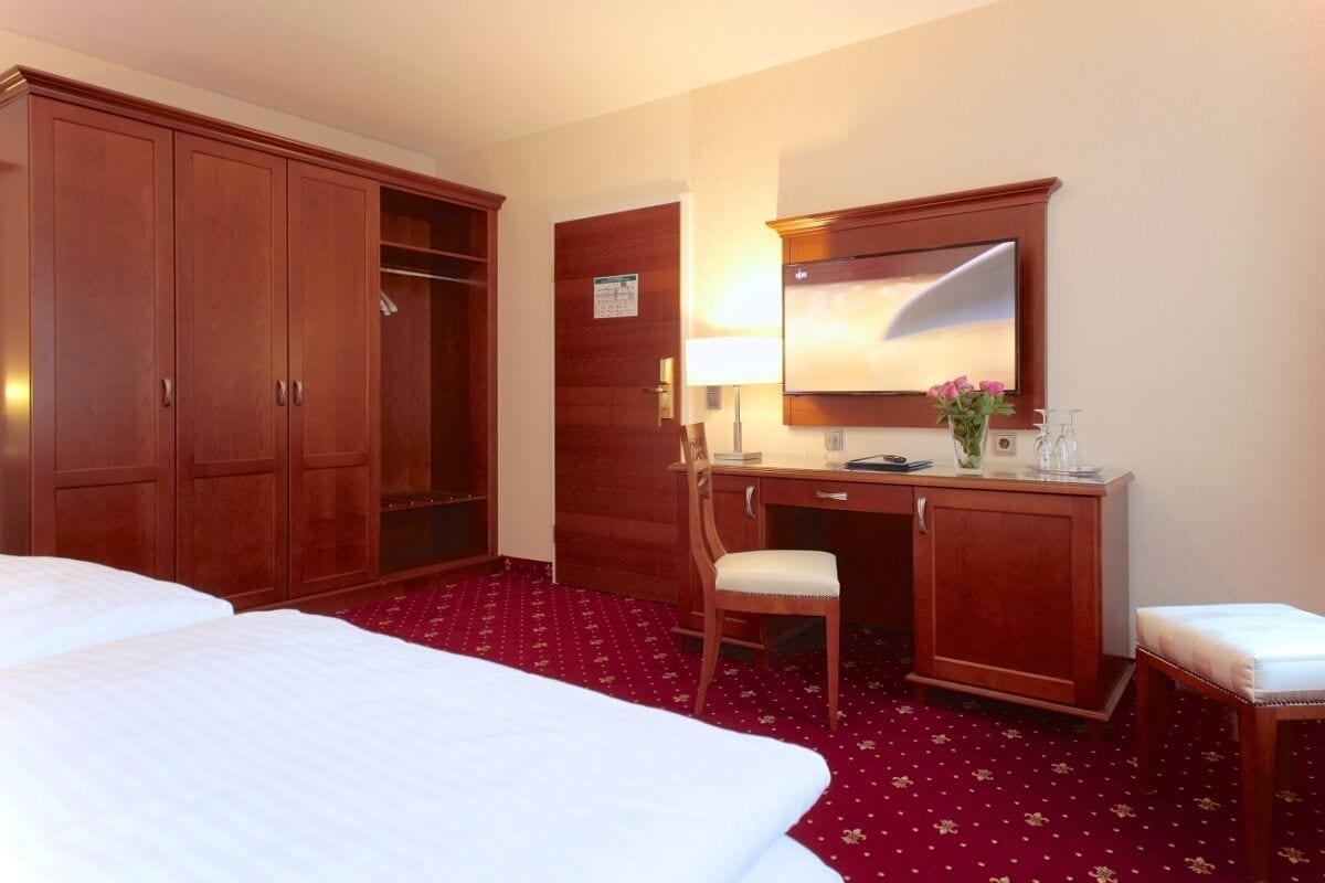 A hotel room with two beds, a desk with a chair, a wardrobe, and a mirror.