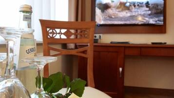 A hotel room with a wooden desk, a television, and a table with a glass bottle and a white rose.