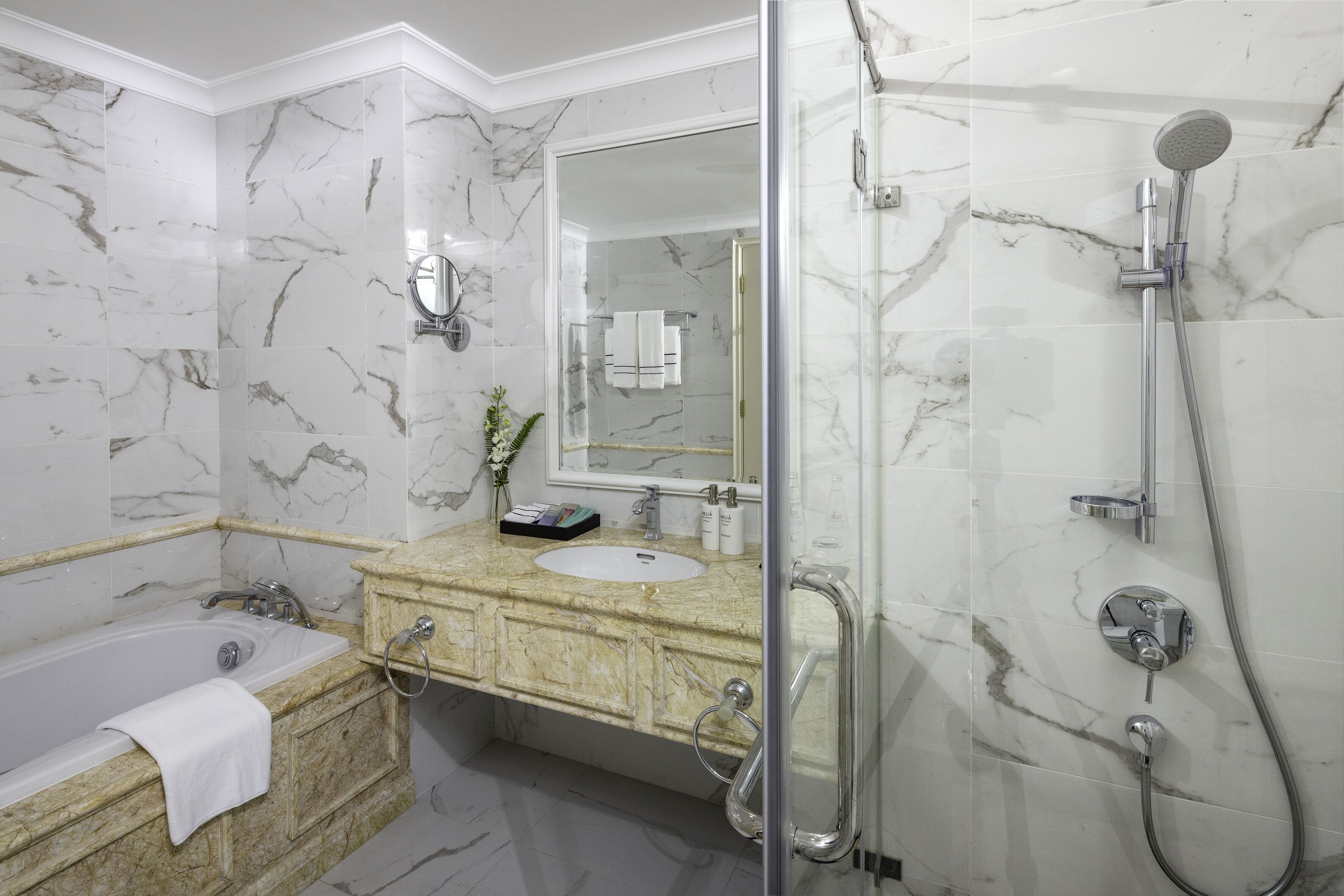 A bathroom with a marble-tiled wall, a sink with a vanity, a bathtub, a glass-enclosed shower, and a mirror.