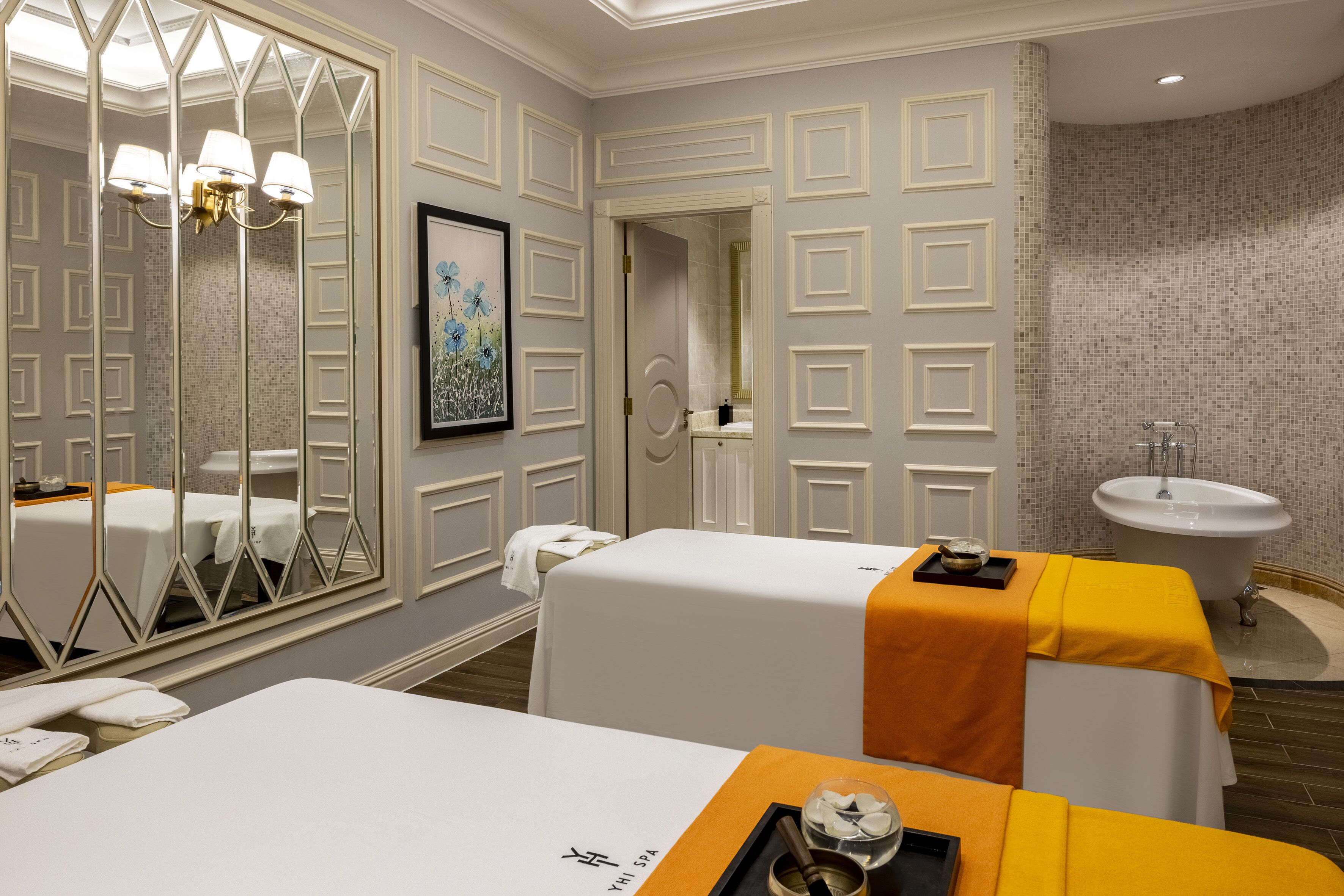 Een spa-ruimte met twee massagetafels, een grote spiegel, een wastafel en een lijstwerk aan de muur.