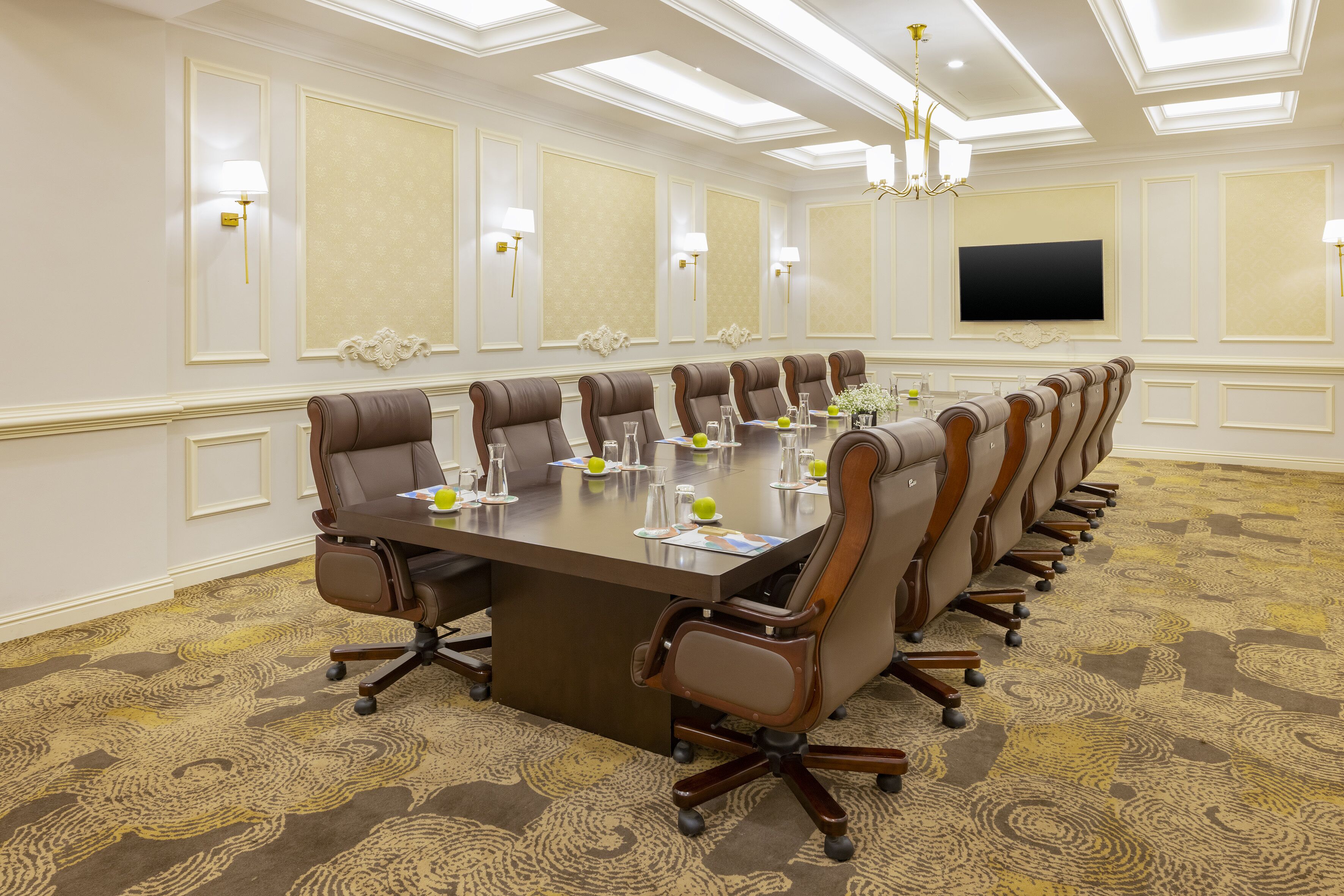 A conference room with a long table, multiple chairs, and a flat-screen TV on the wall.