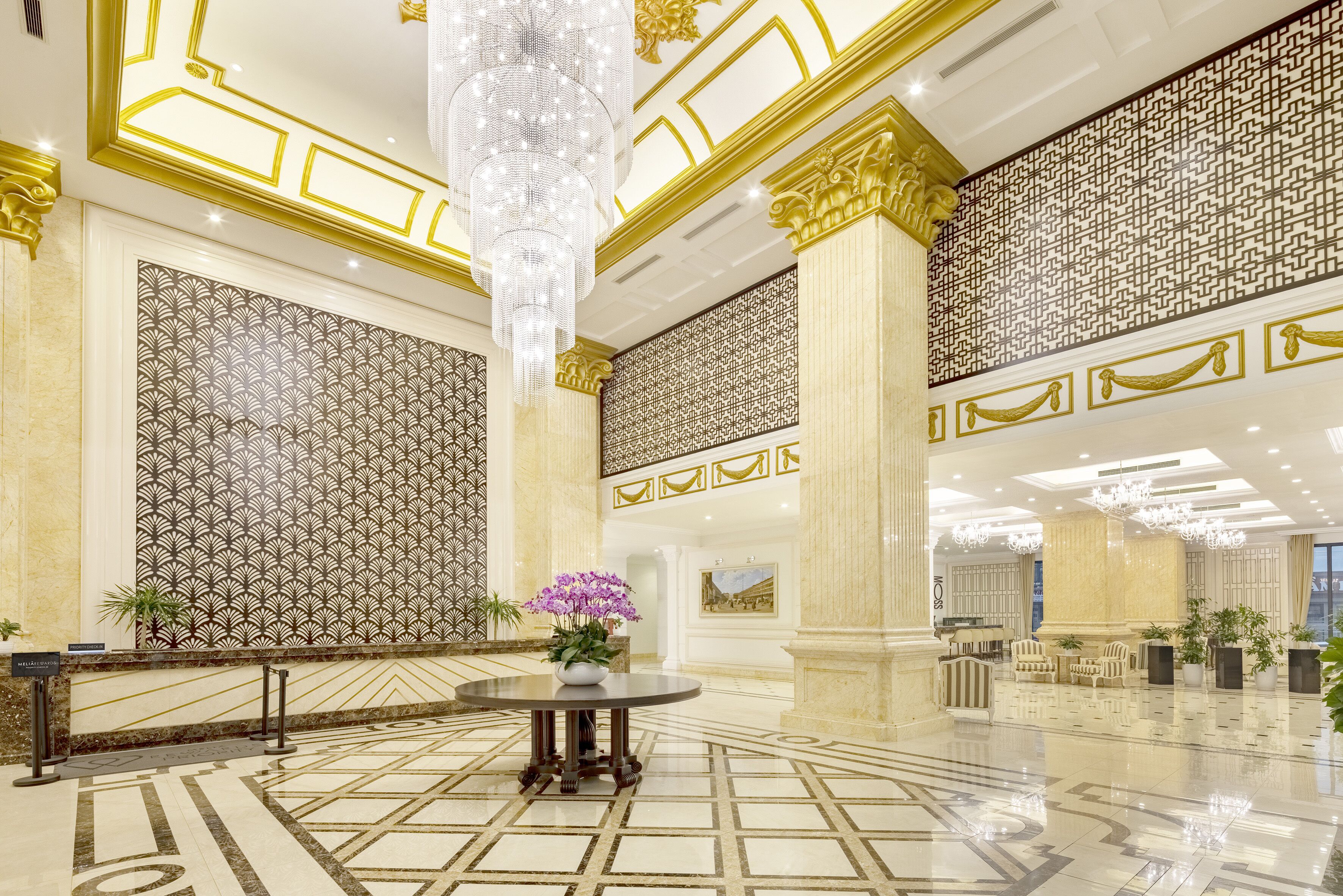 A spacious lobby with a high ceiling, ornate columns, patterned walls, and a central round table with a floral arrangement.