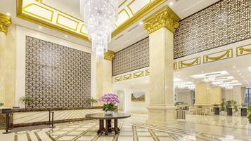 A spacious lobby with a high ceiling, ornate columns, patterned walls, and a central round table with a floral arrangement.