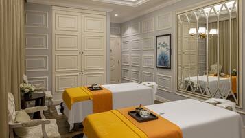A spa room with two beds, a massage table, a chair, and a large mirror.