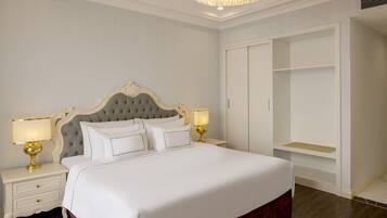A neatly arranged bedroom with a large bed, two bedside tables with lamps, a wardrobe, and a chandelier.