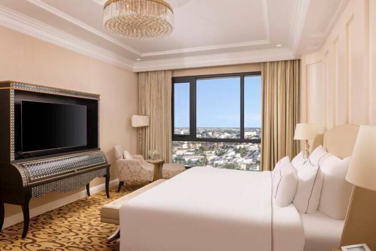 Une chambre d’hôtel avec un grand lit, une télévision, un piano et une vue sur la ville.