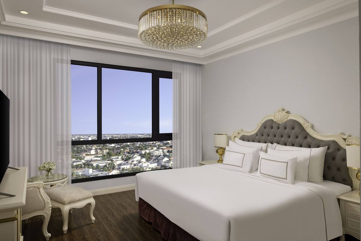 Une chambre d’hôtel avec un grand lit, une vue sur la ville, un lustre et un décor classique.