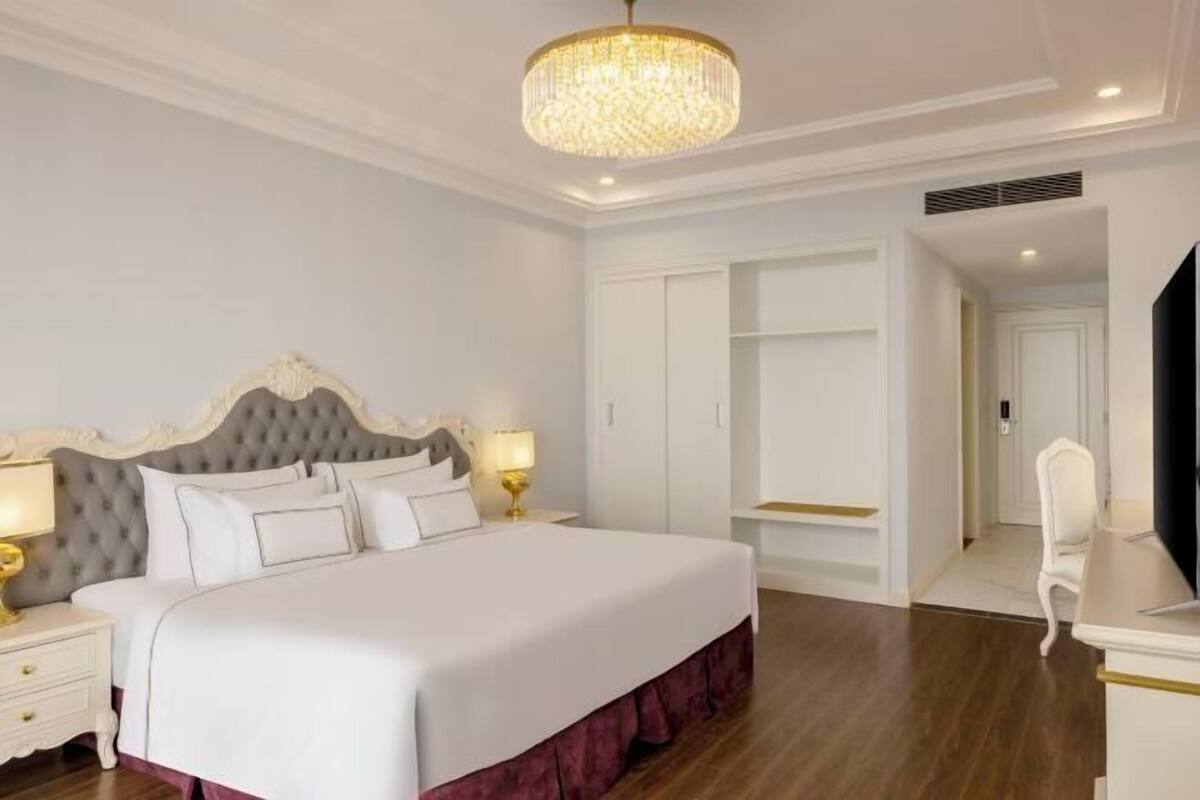 Une chambre d’hôtel avec un grand lit, un lustre, une armoire et un téléviseur.