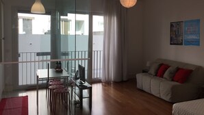 Un salon moderne avec une cloison en verre, un coin repas avec une table et des chaises, un canapé avec des coussins rouges et un luminaire suspendu.