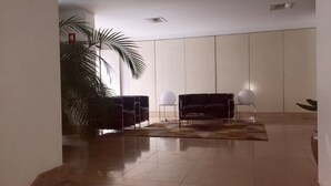 Un hall d’entrée spacieux, avec un canapé noir, deux lampes sphériques blanches et une grande plante en pot.